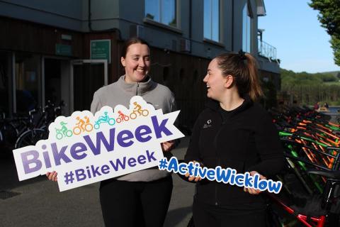 Photo of two women holding signs that say Bike Week #BikeWeek and Active Wicklow