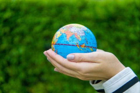 Hands holding a model of planet earth with green outdoor background