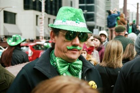 Photo of man with green hat, green bowtie, green moustache and sunglasses as St. Patrick's Day parade